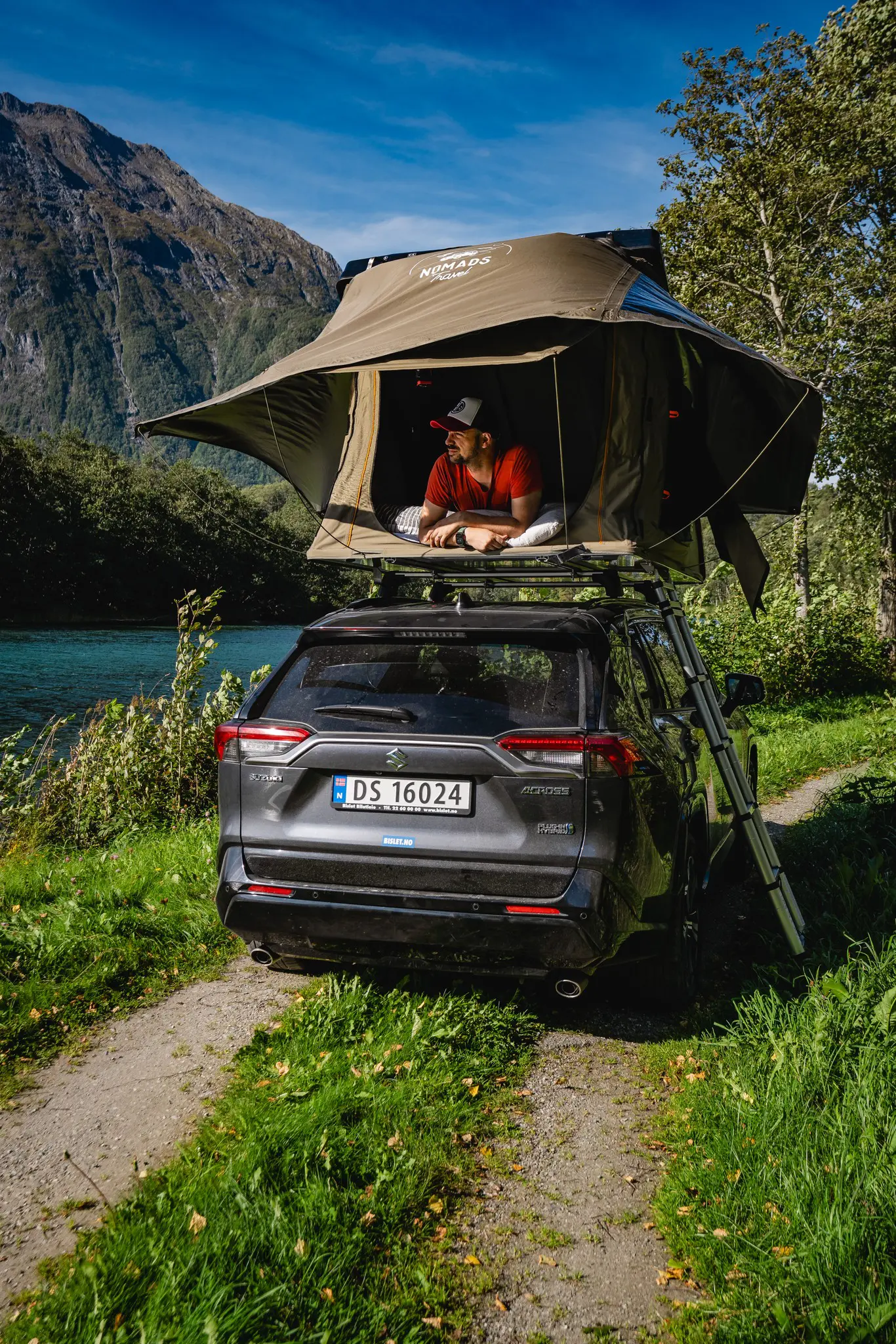 man relaxing in rooftop tent on car by river in Norway mountains